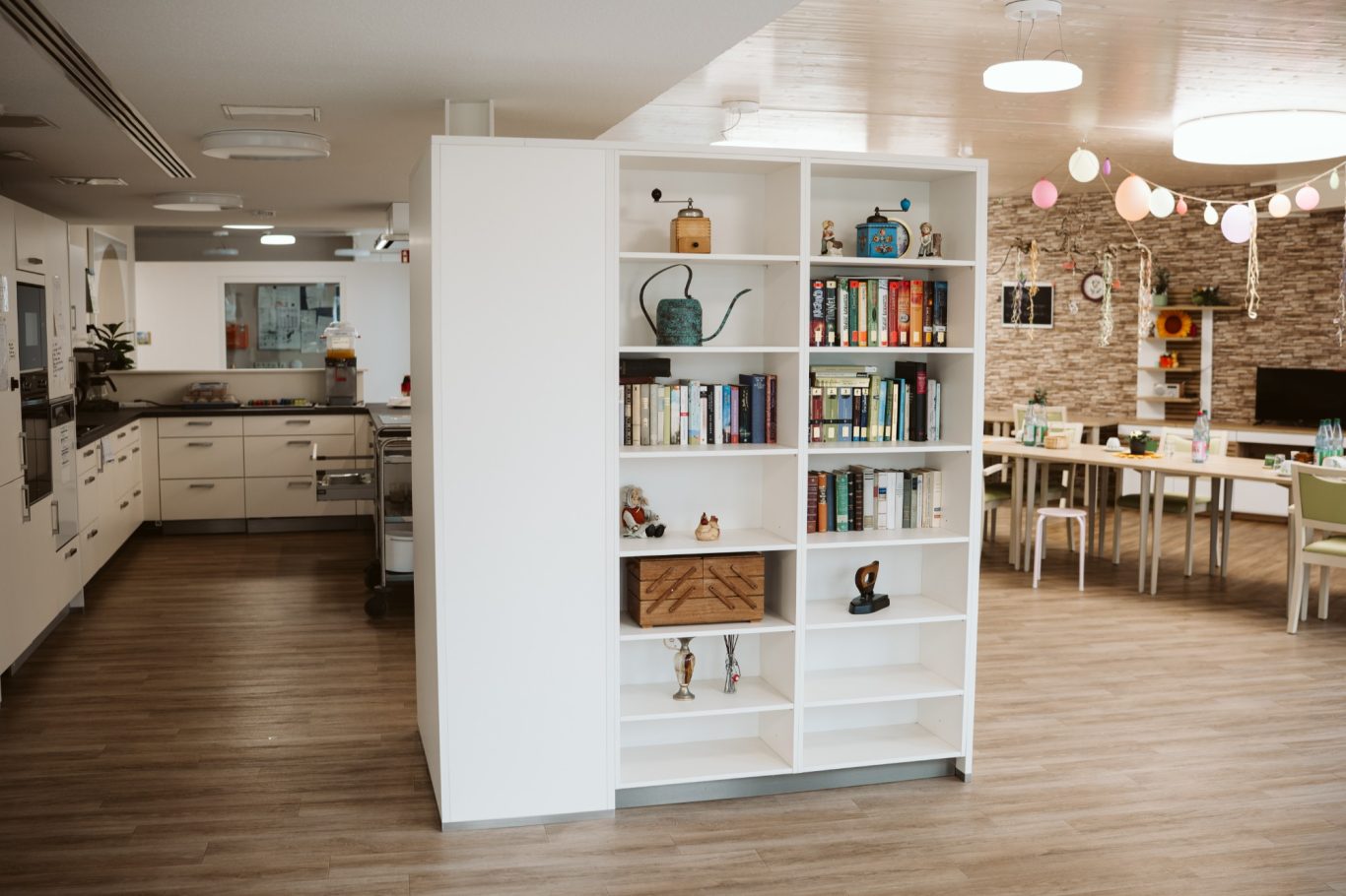 Helles Wohnzimmer mit Buchregal, Essbereich und moderner Kücheneinrichtung.