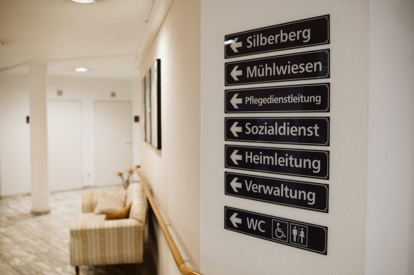 Wegweiser mit beschrifteten Richtungsanzeigen zu verschiedenen Dienstleistungen in einem Flur.