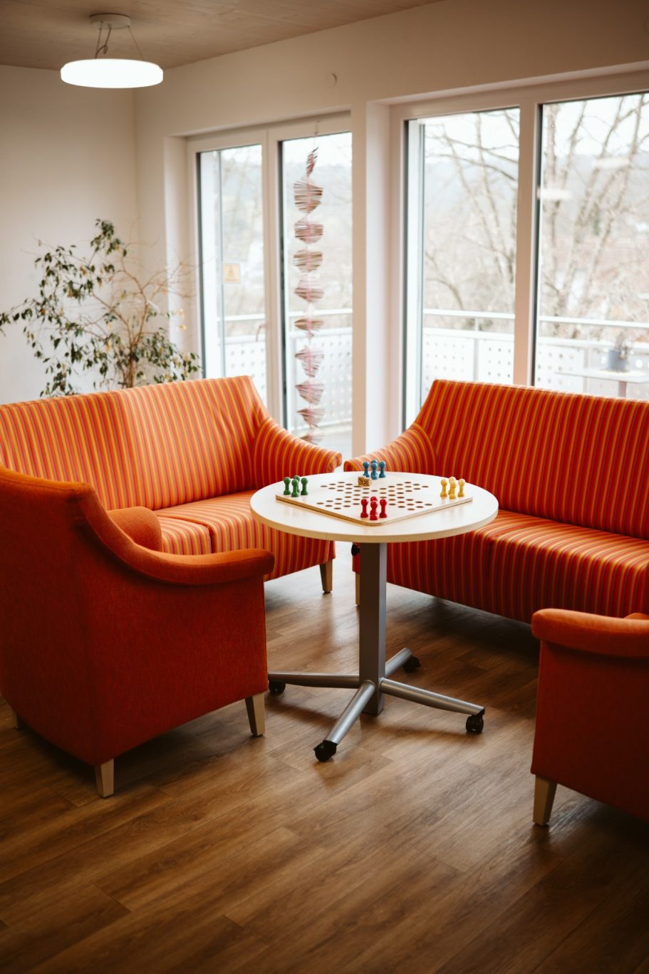Zwei orangefarbene Sofas und ein runder Tisch in einem hellen Raum mit Fenstern.