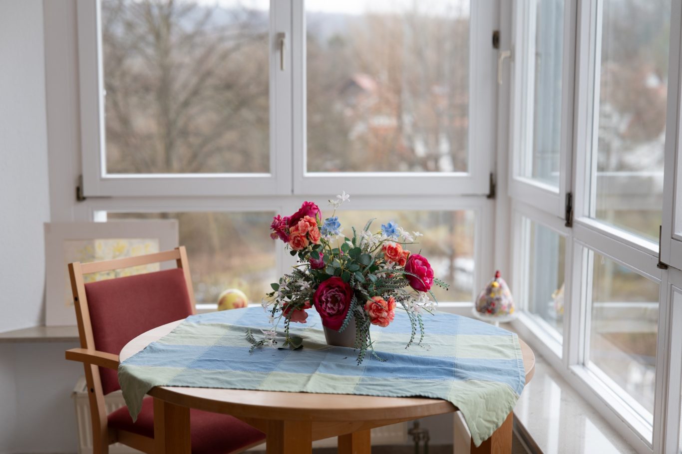 Blumenvase auf einem Tisch mit kariertem Tischdecke und einem Stuhl im Hintergrund.
