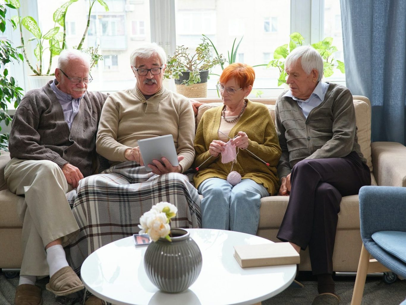 Vier ältere Menschen sitzen auf einer Couch, schauen gemeinsam auf ein Tablet.