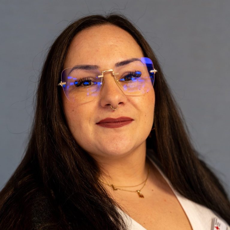 Porträt einer Frau mit langen, dunklen Haaren und blauen Brillengestellen.