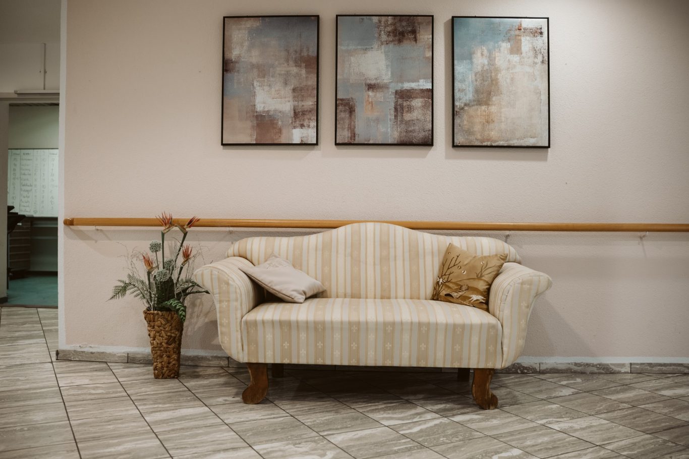 Beige Sofa mit Kissen vor einer Wand mit drei dekorativen Bildern und einer Pflanze.