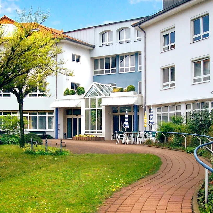 Moderne Gebäude mit Garten, Sitzgelegenheiten und Bäumen im Vordergrund.