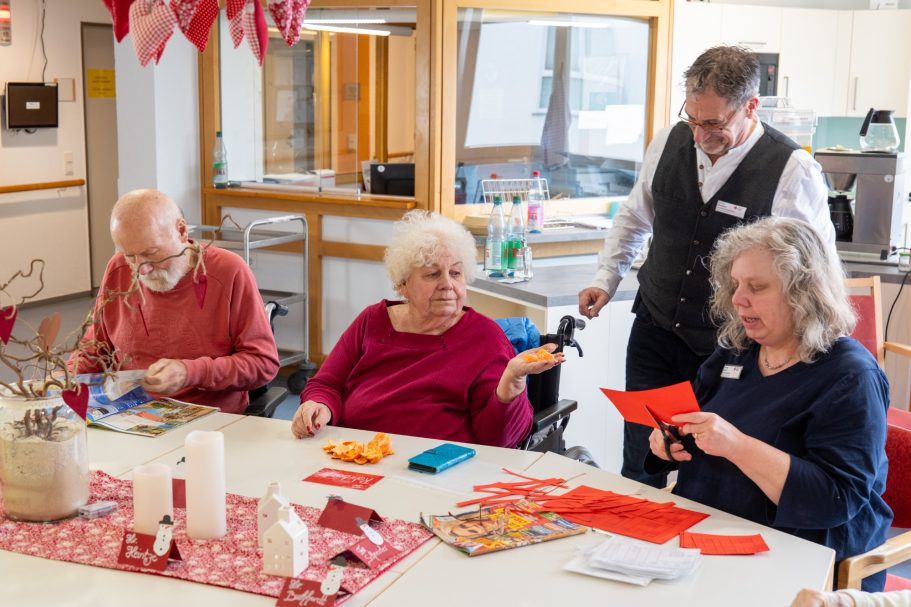 Vier Personen sitzen an einem Tisch, basteln mit buntem Papier und haben Freude am kreativen Arbeiten.