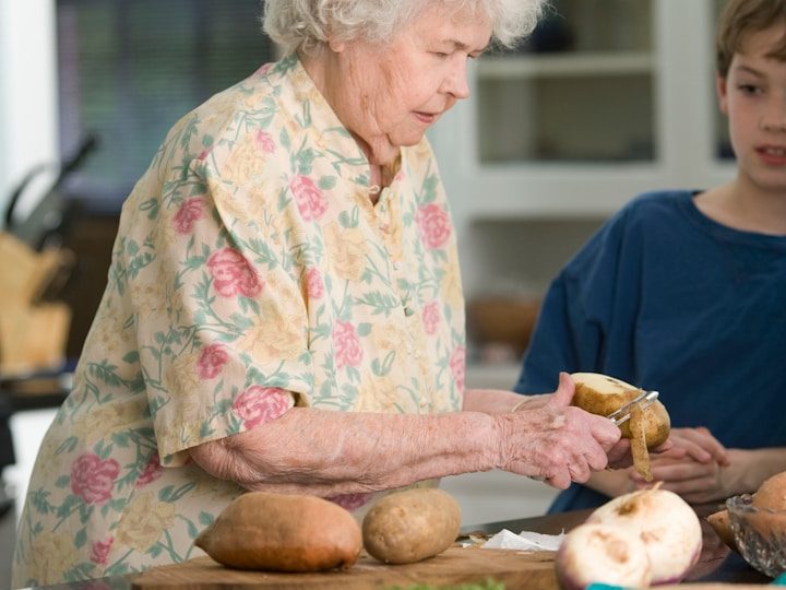 Eine ältere Frau schält Kartoffeln, während ein Junge ihr zusieht.